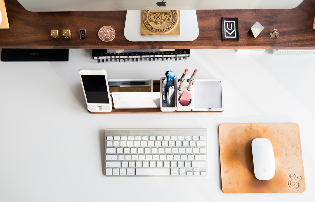 Uma mesa de home office onde teclado, mouse, celular, canetas, e diversos acessórios estão perfeitamente distribuídos simetricamente